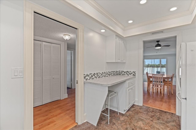 kitchen with white cabinets, light countertops, ornamental molding, freestanding refrigerator, and a tray ceiling