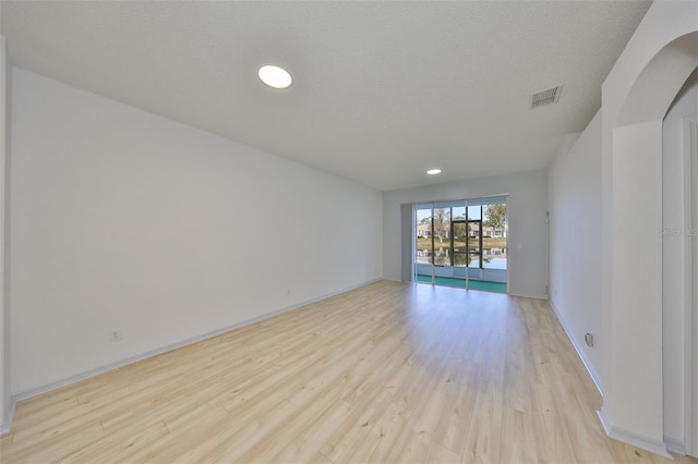 empty room with baseboards, a textured ceiling, visible vents, and light wood-style floors