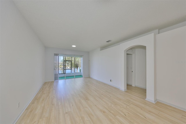 spare room featuring baseboards, visible vents, arched walkways, a textured ceiling, and light wood-type flooring