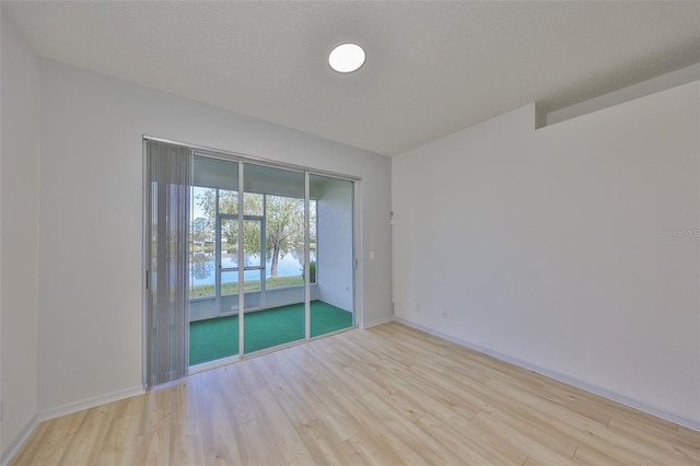 empty room with baseboards, a textured ceiling, and light wood-style floors