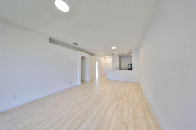 unfurnished living room with arched walkways, light wood-type flooring, visible vents, and baseboards