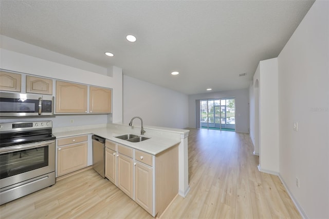 kitchen with a peninsula, stainless steel appliances, light countertops, light brown cabinets, and a sink