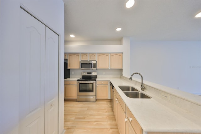 kitchen with stainless steel appliances, a sink, light countertops, light wood-type flooring, and light brown cabinetry