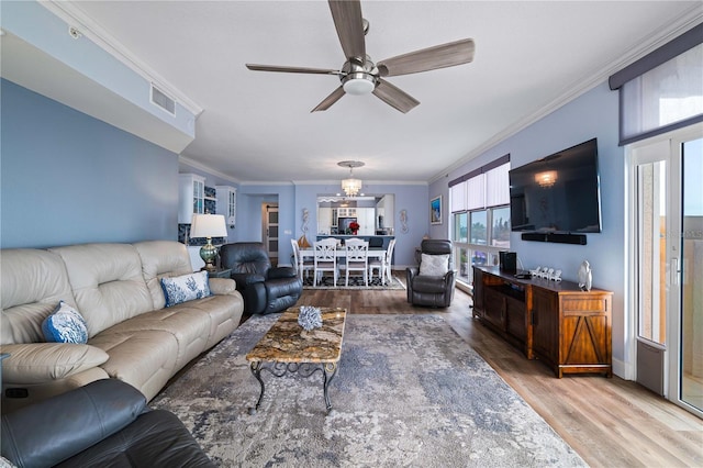 living area featuring wood finished floors, ceiling fan with notable chandelier, visible vents, and ornamental molding