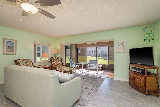 living area featuring a sunroom, baseboards, a ceiling fan, and a textured ceiling