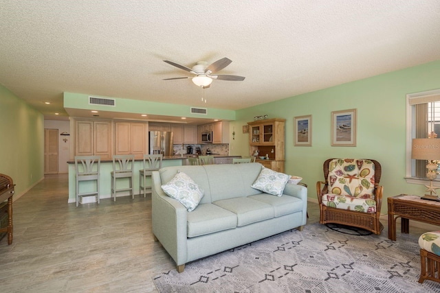 living room with a ceiling fan, visible vents, and a textured ceiling