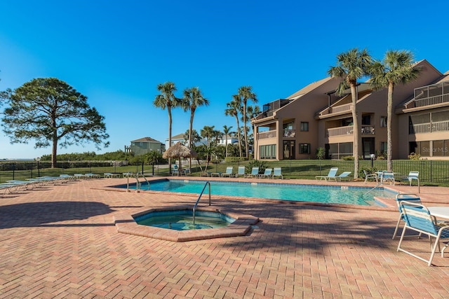 community pool with a patio area, a hot tub, and fence