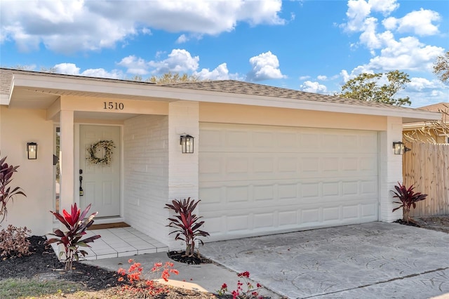 property entrance featuring concrete driveway, brick siding, fence, and an attached garage