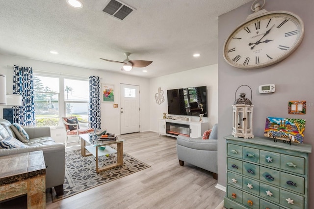 living room featuring a textured ceiling, a glass covered fireplace, wood finished floors, and visible vents