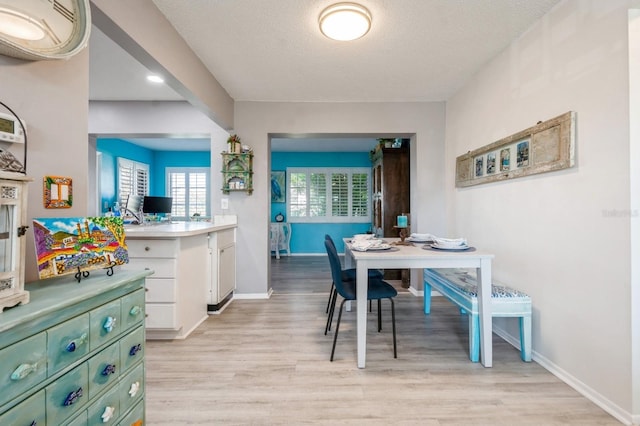 dining space with light wood-style floors, baseboards, and a textured ceiling