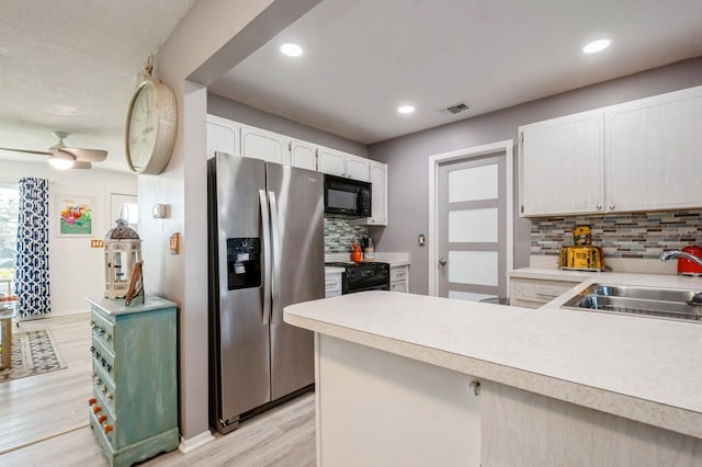 kitchen with light wood finished floors, visible vents, a sink, a peninsula, and black appliances