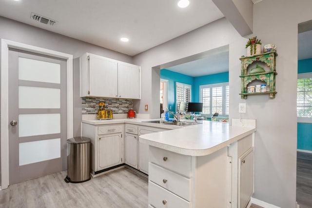 kitchen featuring a peninsula, a sink, visible vents, light countertops, and backsplash