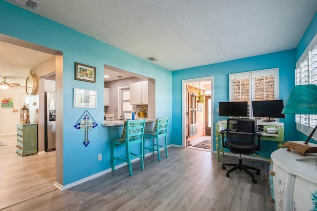 office with visible vents, a textured ceiling, baseboards, and wood finished floors