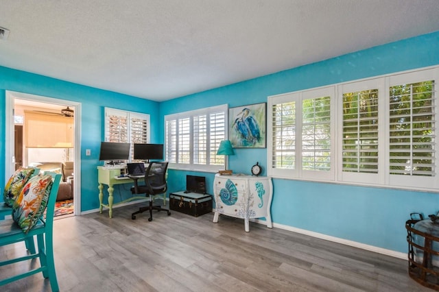 home office with a textured ceiling, wood finished floors, visible vents, and baseboards