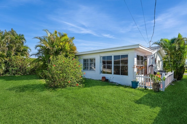 rear view of property with a yard, fence, and stucco siding