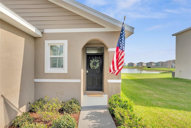 doorway to property featuring stucco siding, a water view, and a lawn