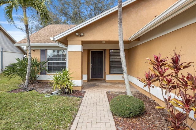 property entrance featuring a shingled roof, a lawn, and stucco siding