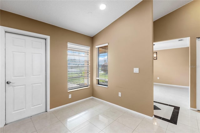 spare room with lofted ceiling, light tile patterned flooring, and baseboards