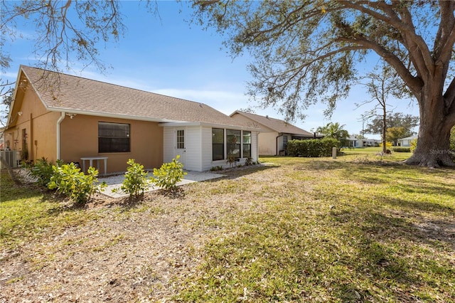 back of house with stucco siding, a shingled roof, central air condition unit, a lawn, and a patio area