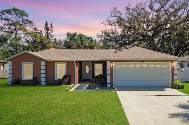 ranch-style house with driveway, roof with shingles, an attached garage, a yard, and stucco siding