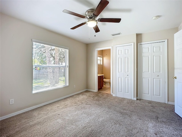 unfurnished bedroom featuring ensuite bathroom, light carpet, a ceiling fan, visible vents, and multiple closets