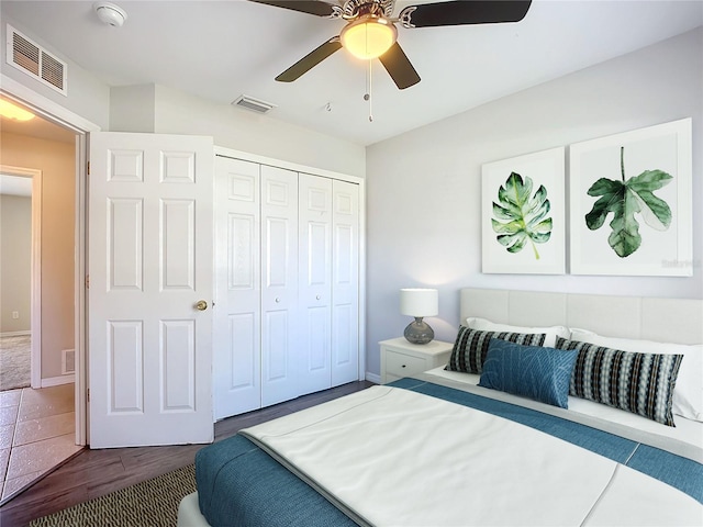 bedroom with ceiling fan, visible vents, dark wood-style flooring, and a closet