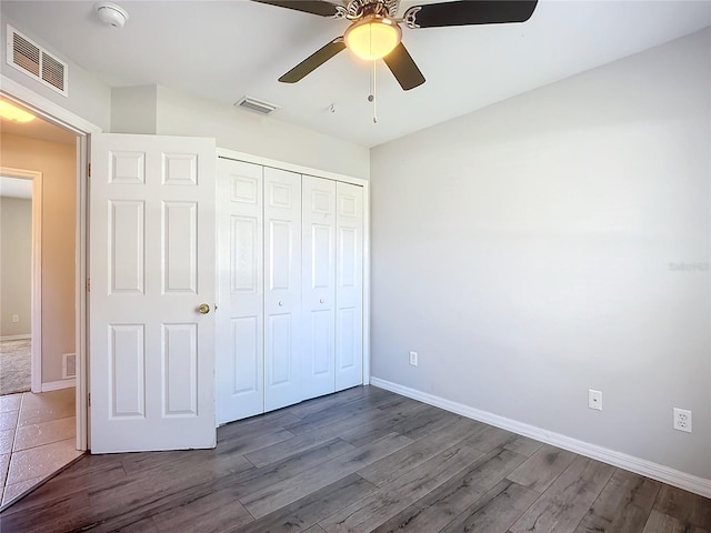 unfurnished bedroom with dark wood-style floors, a closet, visible vents, and baseboards