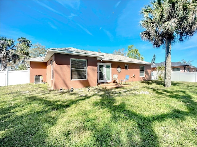 rear view of property with stucco siding, a fenced backyard, a yard, and central AC unit