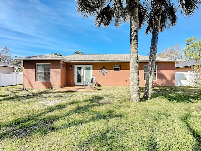 rear view of house with a yard, fence, french doors, and stucco siding