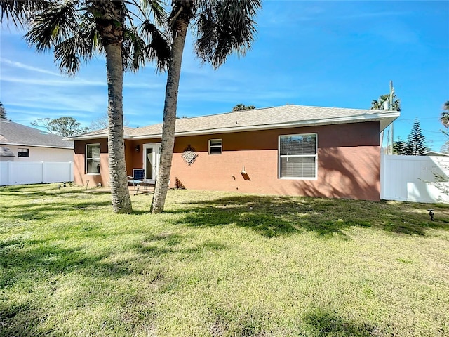 rear view of house featuring fence, a lawn, and stucco siding