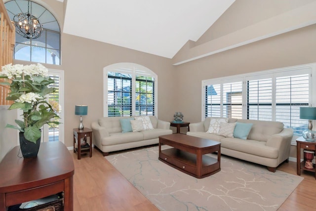 living area with a chandelier, high vaulted ceiling, wood finished floors, and baseboards