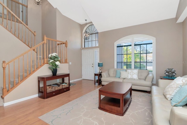 living area with stairway, a high ceiling, an inviting chandelier, wood finished floors, and baseboards