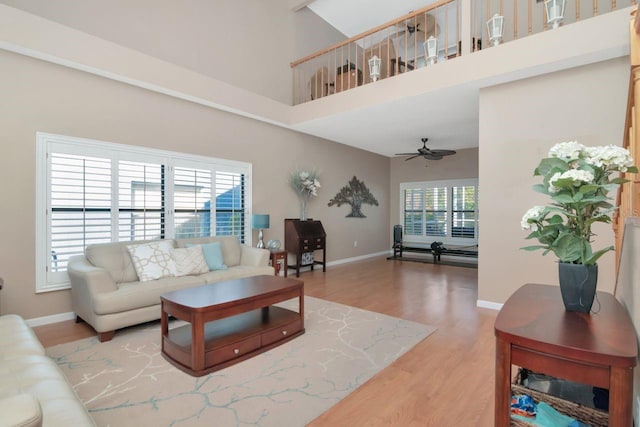 living area featuring ceiling fan, wood finished floors, a towering ceiling, and baseboards