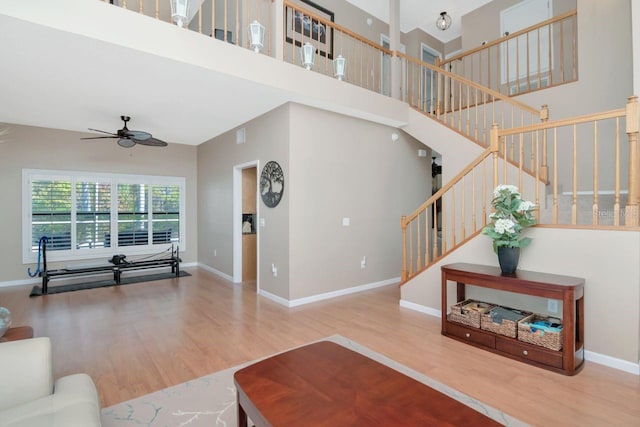 living room featuring a ceiling fan, stairway, baseboards, and wood finished floors