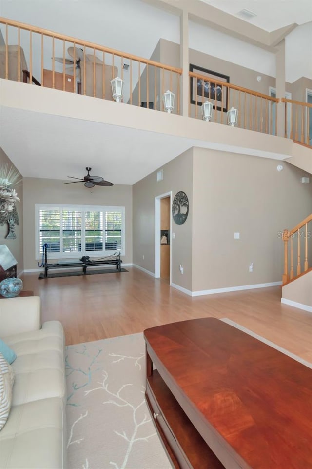 living room featuring a high ceiling, a ceiling fan, wood finished floors, baseboards, and stairs