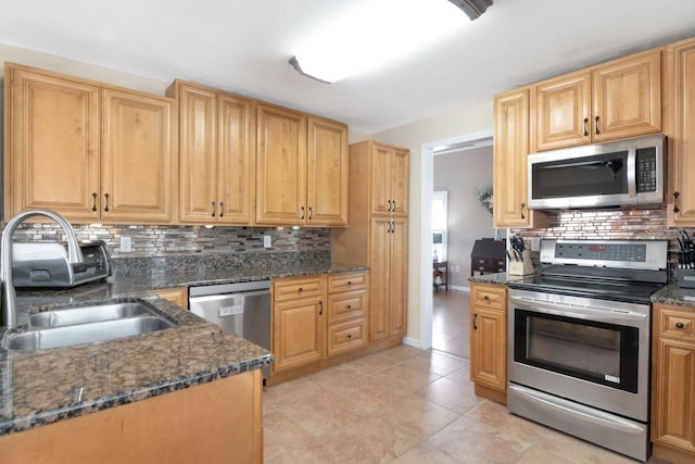 kitchen featuring dark stone counters, stainless steel appliances, backsplash, and a sink