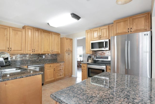 kitchen featuring light tile patterned floors, stainless steel appliances, a sink, tasteful backsplash, and dark stone countertops