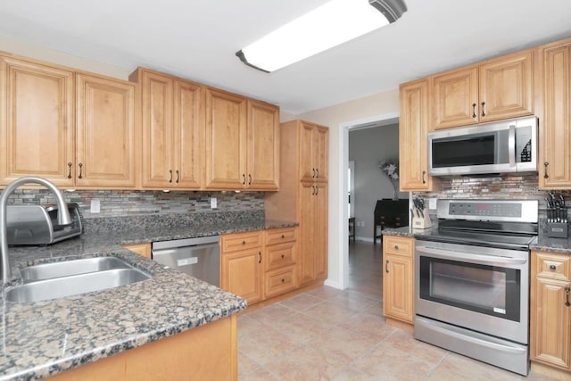 kitchen featuring tasteful backsplash, appliances with stainless steel finishes, stone countertops, a sink, and baseboards