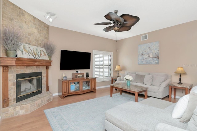 living area with ceiling fan, a fireplace, wood finished floors, visible vents, and baseboards