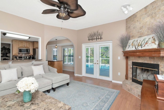 living area with a large fireplace, french doors, light wood-type flooring, and baseboards