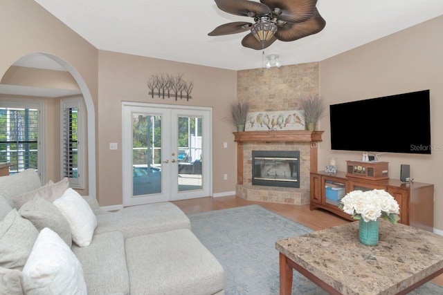 living room with ceiling fan, a large fireplace, wood finished floors, baseboards, and french doors