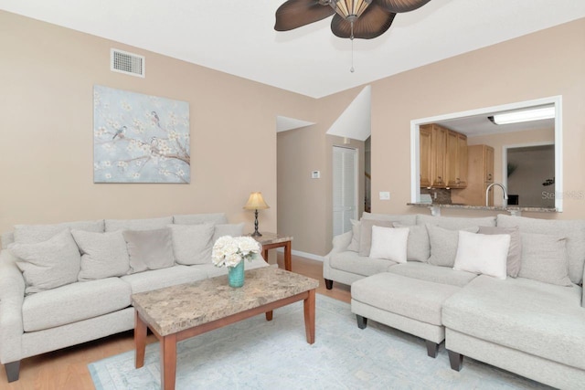 living room with light wood finished floors, a ceiling fan, visible vents, and baseboards