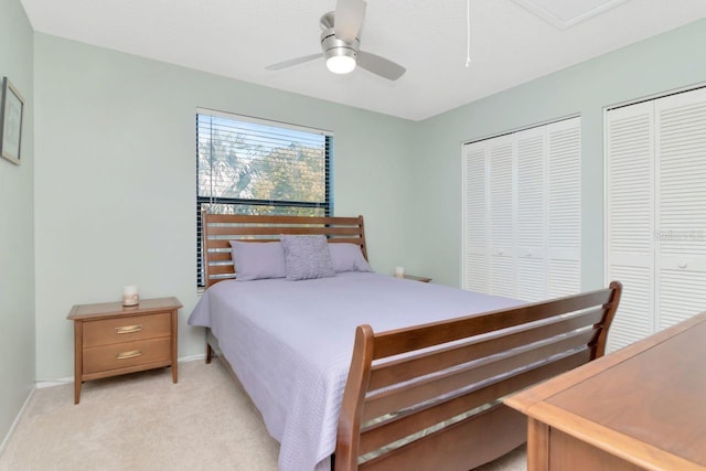 bedroom with multiple closets, light colored carpet, attic access, ceiling fan, and baseboards