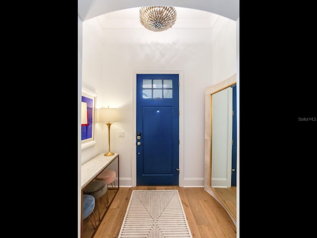 entryway featuring light wood-style floors, baseboards, arched walkways, and ornamental molding