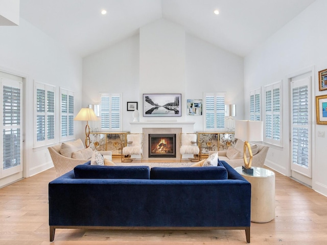 living room featuring high vaulted ceiling, light wood-type flooring, a high end fireplace, and baseboards