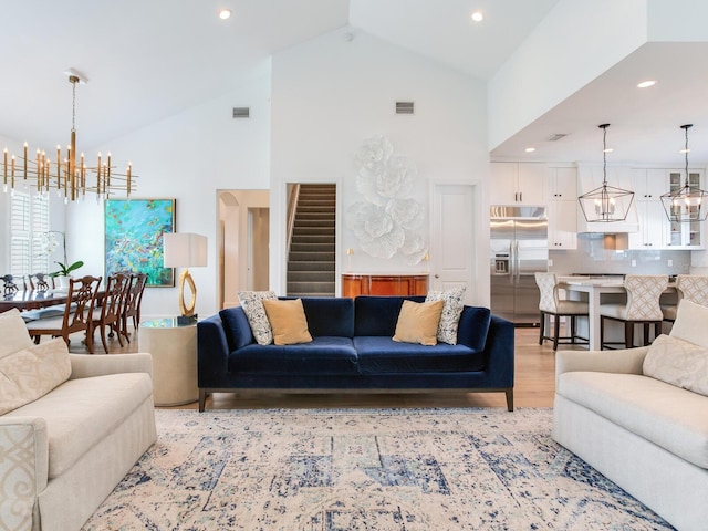 living area with an inviting chandelier, visible vents, light wood finished floors, and high vaulted ceiling