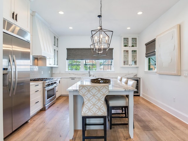 kitchen featuring stainless steel appliances, custom range hood, white cabinets, a kitchen island, and light stone countertops