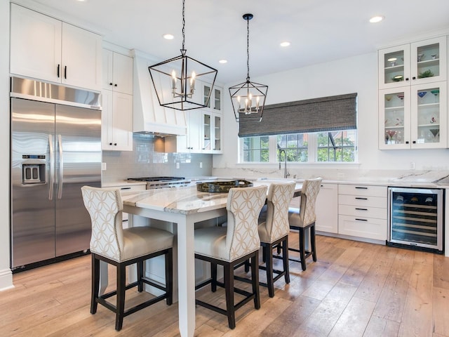 kitchen featuring custom range hood, wine cooler, light stone countertops, stainless steel built in fridge, and light wood-type flooring