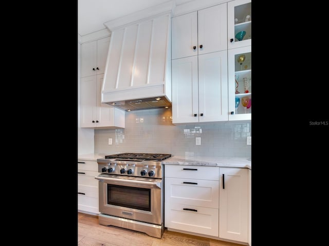 kitchen featuring stainless steel range, white cabinets, decorative backsplash, glass insert cabinets, and light stone countertops