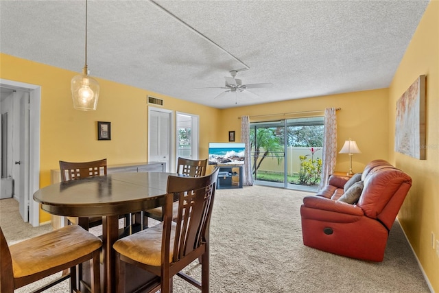 carpeted dining room featuring a textured ceiling, a ceiling fan, visible vents, and baseboards